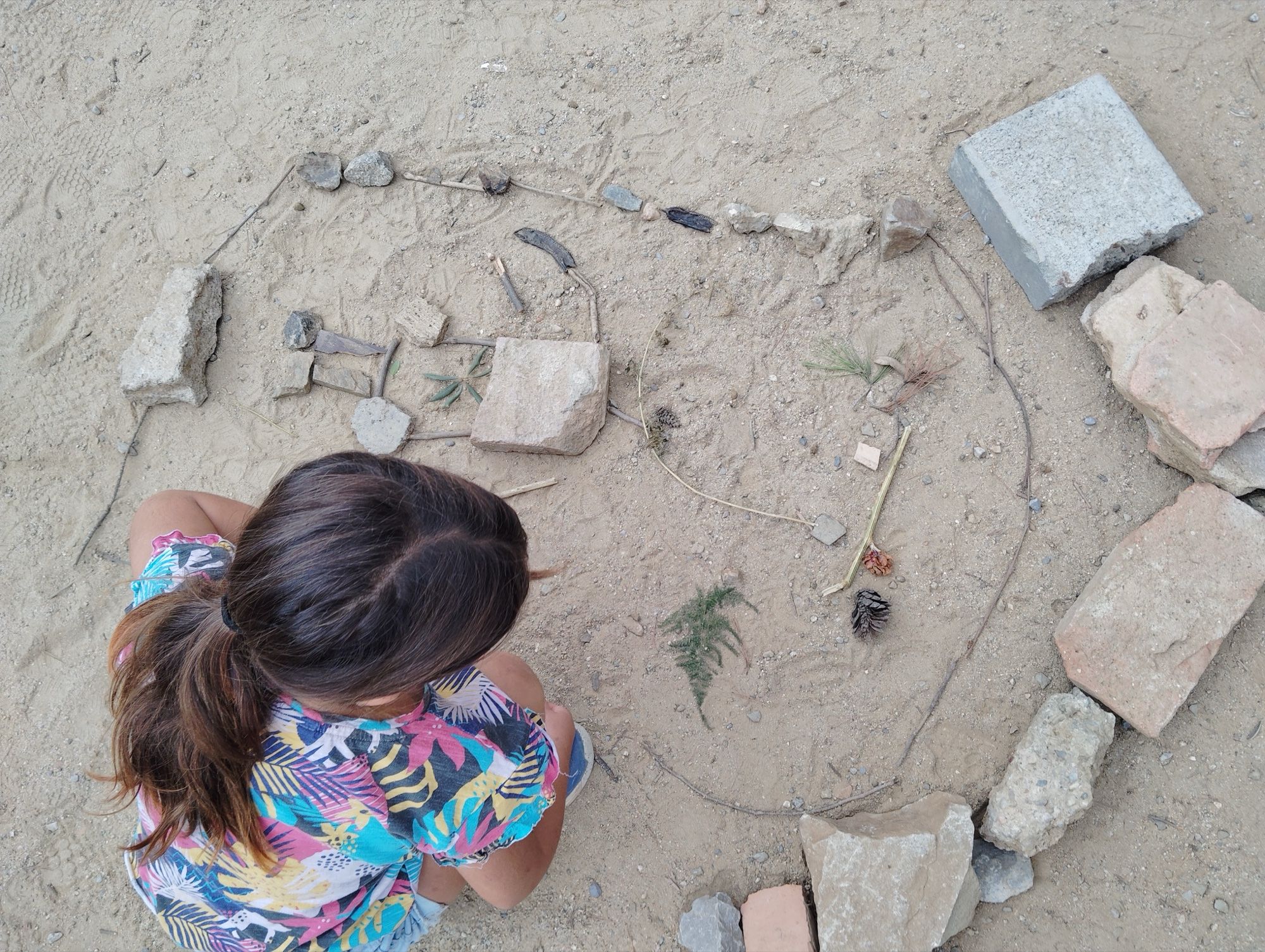 Land art in the playground: a child seen from above arranges stones, twigs and pine cones