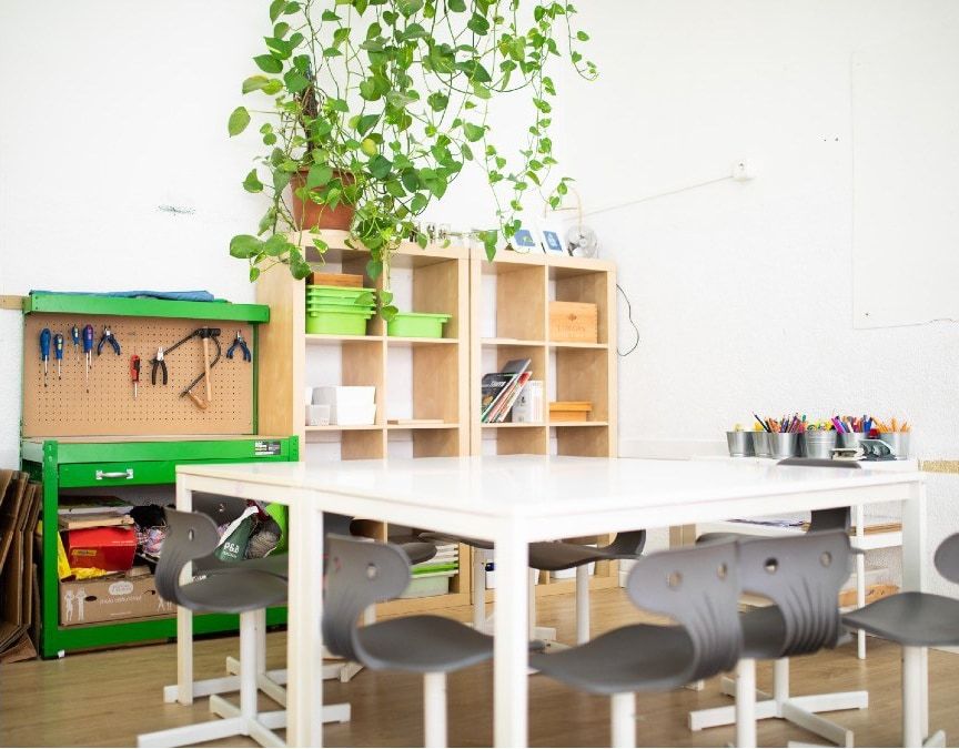 Taller de l’escola amb plantes penjades i material de treball a les taules